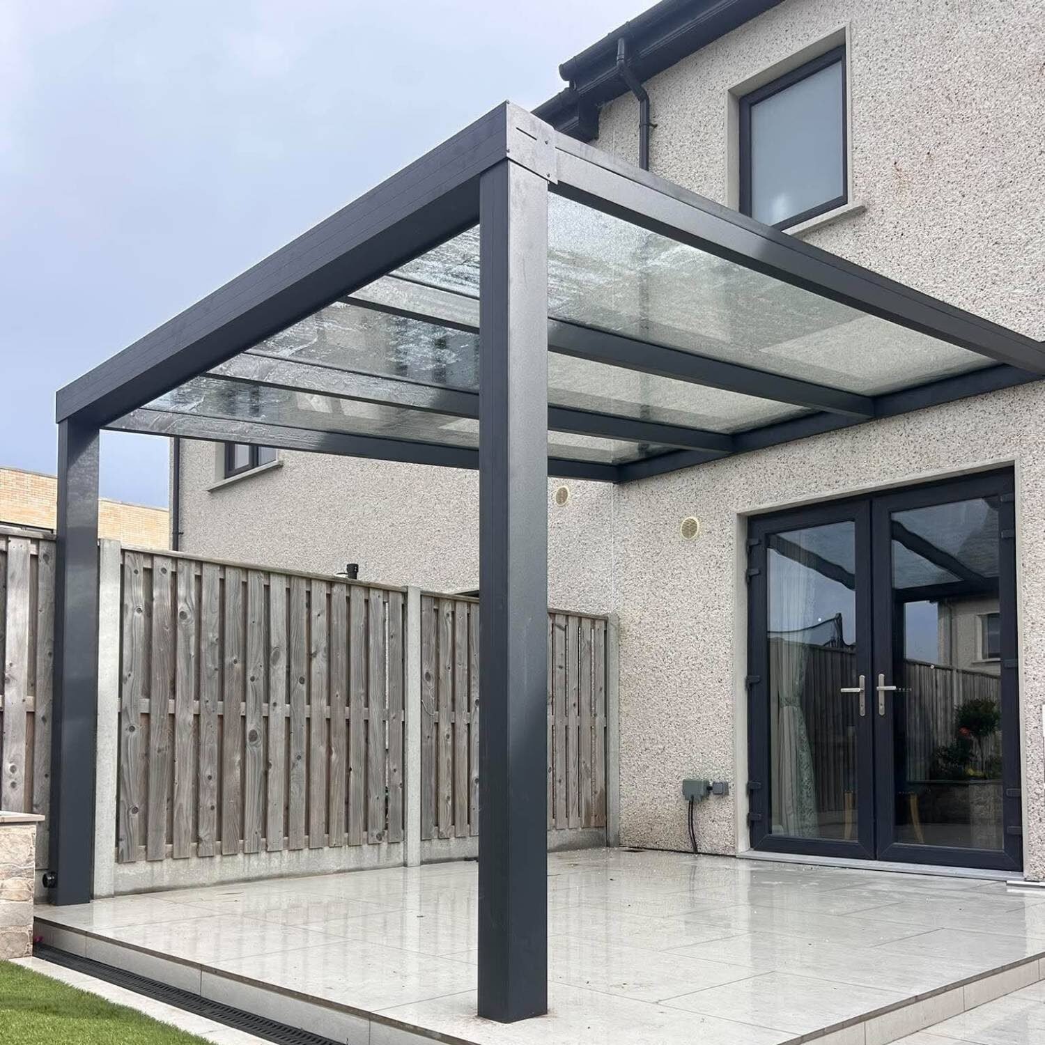 Open aluminium pergola with a clear glass roof over a patio at the back of a house